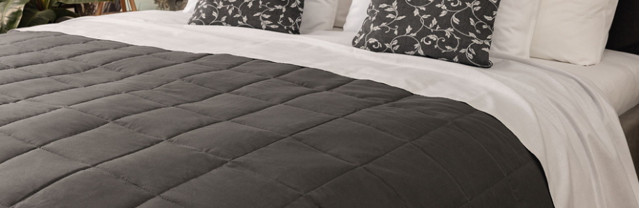 Bett im Hotelzimmer. Auf dem Bett sind Kopfkissen und eine Tagesdecke.